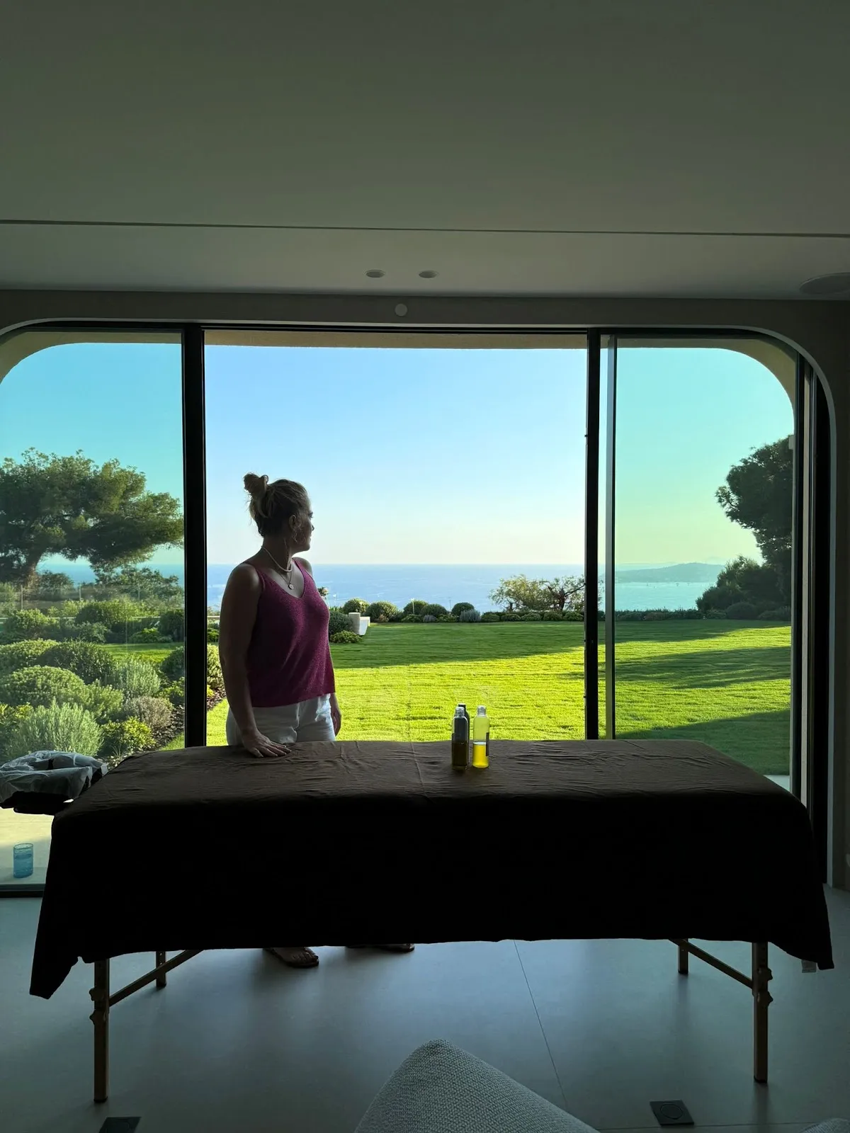 Camille by her massage table in a villa, garden and sea in the background